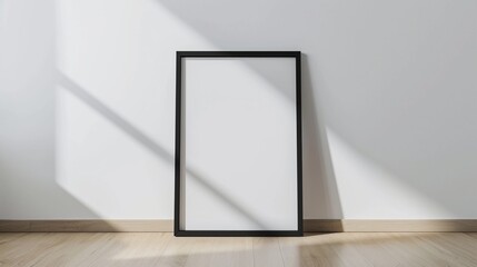 An empty vertical black poster frame stands on a light wooden floor against a white wall. It serves as a blank canvas for a picture frame mockup, offering a clean and minimalist aestheti