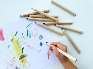 small child draws with colored pencils on paper on white table.