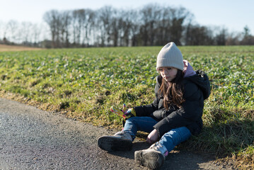 Naklejka na ściany i meble Little girl sitting on the road in the middle of a field of cabbage