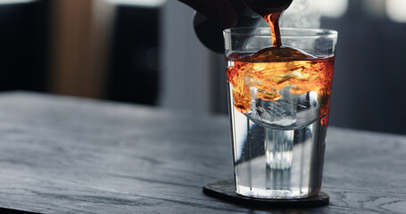 pour tonic water over clear ice ball in tumbler glass on black oak table