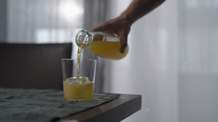 man pour lemonade in tumbler glass with ice cube on wood table