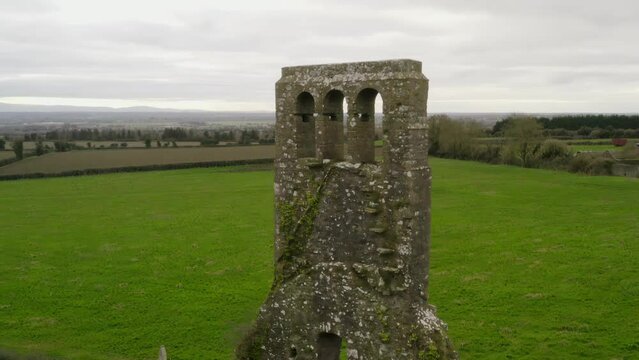 Aerial orbit around brick structure remnants of bell tower at church in green countryside