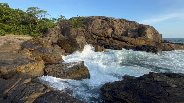 A pristine island on a sunny day, with water crashing against the rocks