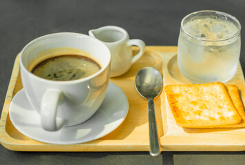 Coffee latte art on a wooden tray with crackers and cold water.