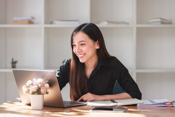 Smiling businesswoman studying and working in a home office environment with books, papers, and a laptop on the table