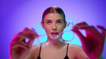 Attractive blonde woman plays with reading glasses in front of the camera and tries them on, close portrait shot in studio with bare torso - Powered by Adobe