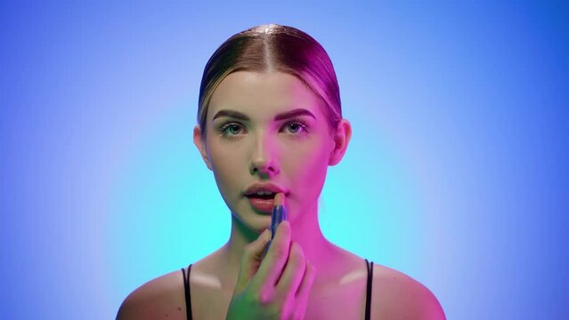 Young caucasian blonde woman with evening makeup puts on lipstick, portrait shot in studio
