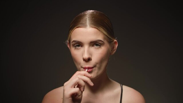 Caucasian Young Blonde Attractive Woman Sucks and Licks Lollipop Candy Close Up Studio Portrait Shot with Infinite Black Background