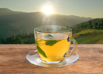 Aromatic green tea in glass cup on wooden table in mountains