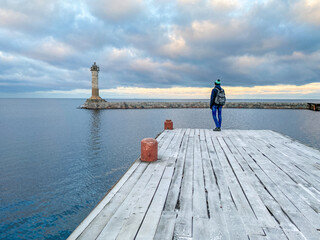 A person stands on a wooden pier and looks at the lighthouse. Concept of travel, achievement,...