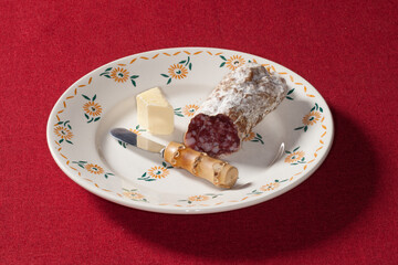 Saucisson entamé, morceau de beurre et petit couteau dans une assiette posée sur une nappe rouge