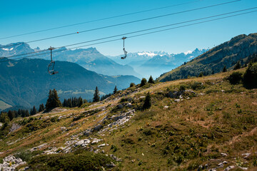 Panoramic view on the Vaud Alps in Switzerland above Leysin, near Aigle, with empty chairlifts and limestone rocks in the foreground and snow-capped mountain peaks in the background