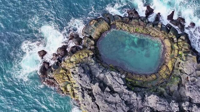 Aerial drone summer view with azimuthal rotating left movement, close-up of the rocky Brimketill Pool with waves in the Reykjanes Peninsula, Iceland.