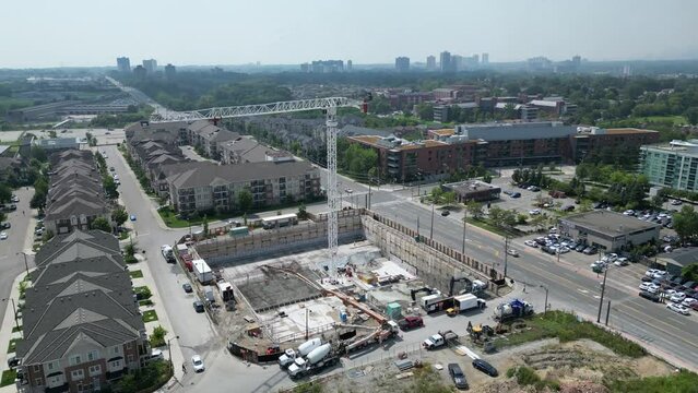 Condo tower crane at development construction site during housing crisis and labour shortage with workers and trucks; drone hyperlapse