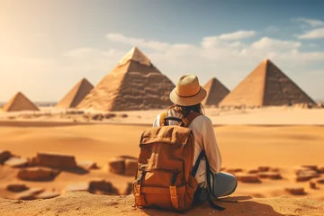 Foto op Canvas A lone tourist with a backpack sits contemplating the ancient pyramids in Egypt under the clear blue sky. © Jsanz_photo