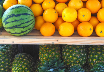 Group of whole ripe pineapples and oranges on a wooden shelf with a melon