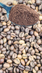 Ground coffee powder in a metal spoon in the foreground, against the background of roasted aromatic coffee beans. Coffee concept.
