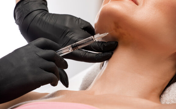 Cosmetologist makes lipolytic injections to burn fat on the chin, cheeks and neck of a woman against double chin. Female aesthetic cosmetology in a beauty salon.Cosmetology concept.