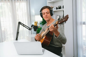 Host channel in smart singer with smiling face, playing guitar along singing, broadcasting on social media channel, wearing headphones to record video streamer at modern studio recording. Pecuniary.