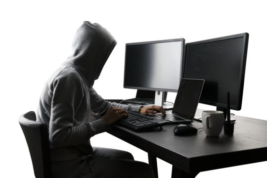 Hooded figure operating computer, dark theme suggesting cybersecurity or hacking activity