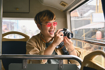 Cheerful man tourist in pink glasses holding camera enjoying the travel on bus