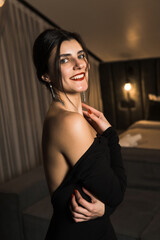 Fototapeta na wymiar Elegant woman in a black dress posing in an apartment. Fashion shooting concept