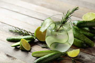 Gin tonic with ice, rosemary, lime, and cucumber on an old wooden table.