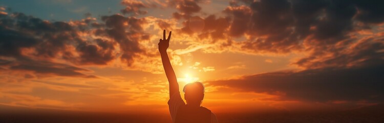 Fototapeta premium silhouette of a man holding up a peace sign at the sunset