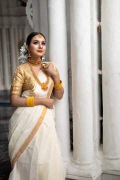 Stunning bride dressed in a traditional Indian bridal saree with gold jewellery smiles tenderly in front of a vintage background. Wedding fashion and lifestyle.