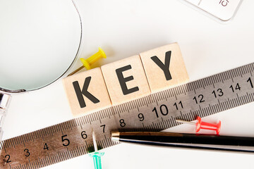 KEY text of non-wooden cubes next to a calculator, pen, measuring ruler, magnifying glass on a white background