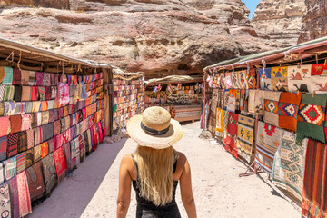 Petra, Jordan - A blonde woman looks at some market stalls where all sorts of things can be bought inside Petra, Jordan. - obrazy, fototapety, plakaty
