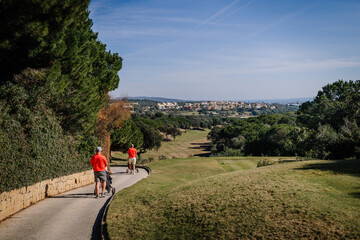 Sotogrante, Spain - January 27, 2024 - Two golfers in red shirts walking on a path with golf bags,...