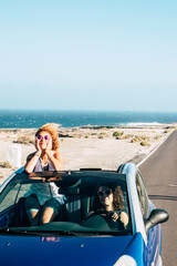 Travel friends and transport with blue convertible car and couple of adult women friends have fun...