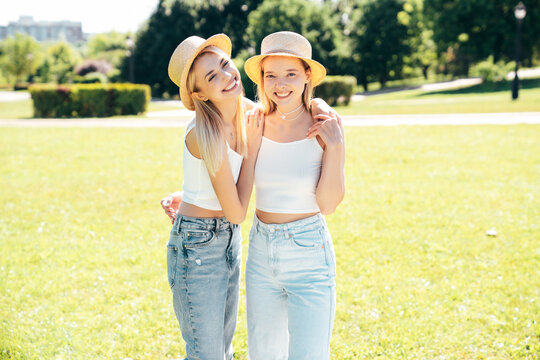Two young beautiful smiling hipster female in trendy summer white t shirt  and jeans clothes. Blond carefree women posing in street. Positive models having fun at sunny day. Going crazy. In park