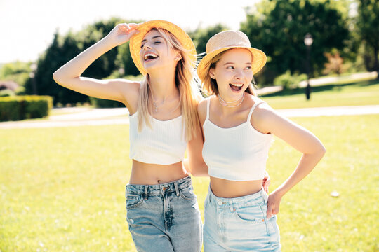 Two young beautiful smiling hipster female in trendy summer white t shirt  and jeans clothes. Blond carefree women posing in street. Positive models having fun at sunny day. Going crazy. In park