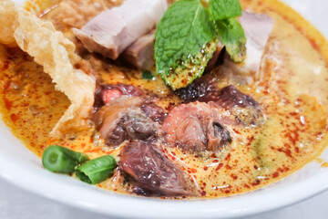 Closeup of delicious curry mee or curry laksa with fresh raw cockerel and roast pork
