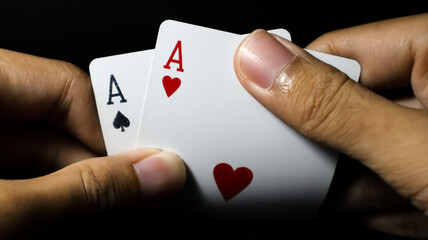 Closeup of a person hand holding a pair of aces against a dark background. Ideal for poker,...
