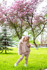 a girl in a light fur coat walks among flowering trees