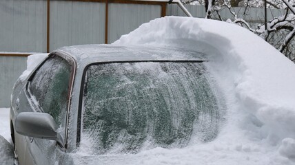 a gray car covered in snow and half cleared of snowdrift, the consequences for transport of a snow...