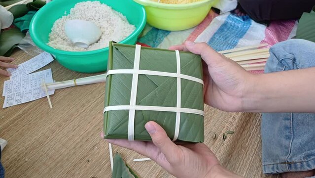Man's hand hold wrapped Banh Chung before cooking, the Vietnamese traditional food made with pork, mung bean, sticky rice, wrapped in green leaves and then boiled.