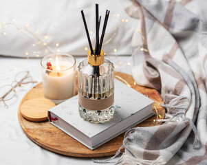 Home fragrance in glass bottle and bamboo sticks with scented candle,  paper book.