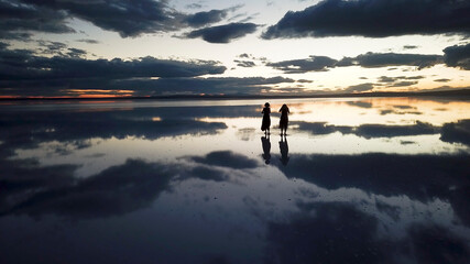  A young two woman dance across the mirror like surface of salt lake as the sun disappears behind the clouds.