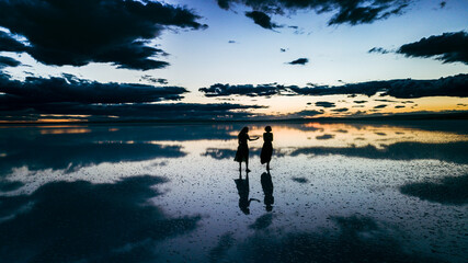  A young two woman dance across the mirror like surface of salt lake as the sun disappears behind...