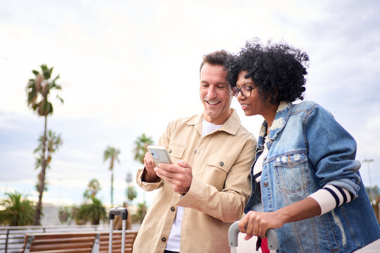 Concentrated Multiracial Mature Tourist Couple Smiling Standing Looking And Using Mobile Phone In Their Hands On Street Tourism City, Searching Location And Enjoying Happy Their Vacation On Sunny Day