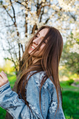Close-up shot of a young woman enjoying herself in a fragrant garden filled with blooming apple and cherry trees during the spring at sunset. A girl playing with her long hair.