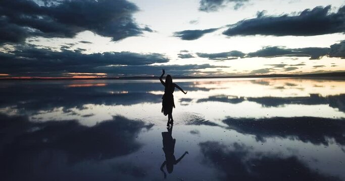 young woman dance across the mirror like surface of salt lake as the sun disappears behind the clouds.