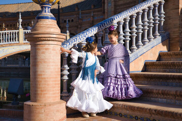 Two girls dancing flamenco looking at each other in typical flamenco costumes on stairs in a beautiful square in Seville. Dance concept, flamenco, typical Spanish, Seville, Spain.