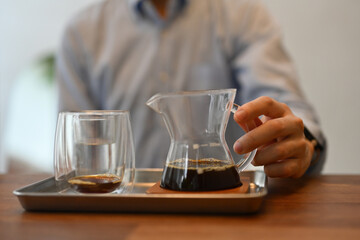 Cropped with a male's hand holding a small glass pitcher with black coffee, Focus on the pitcher