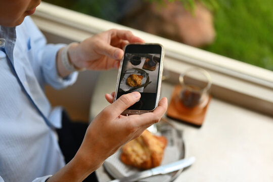 Cropped image of Young Asian man using phone to take a picture of croissant and coffee