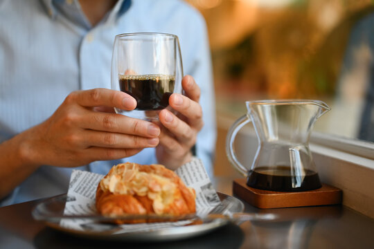 Cropped and close-up image of a Young man enjoying a black coffee and croissant beside the window